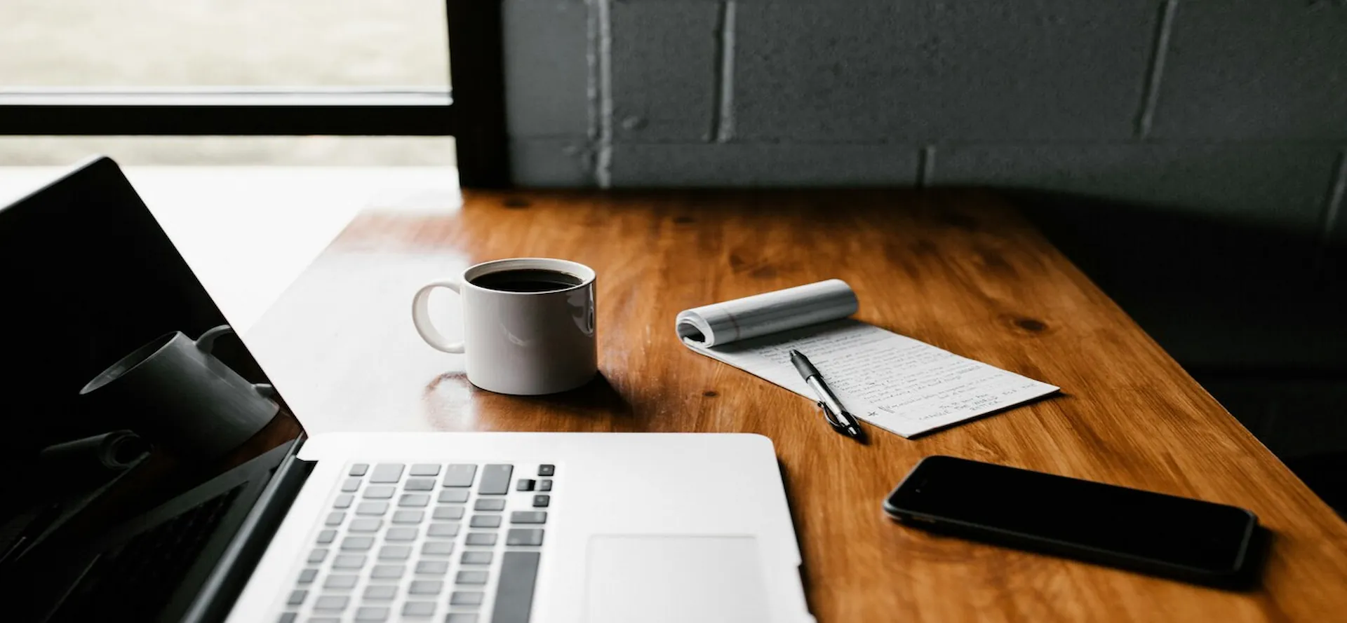 Desk with a notepad, a coffee cup, laptop.