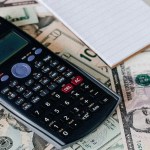 A notebook and a calculator on top of ten dolllar bills